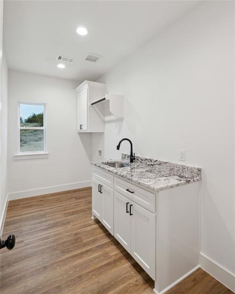 Kitchen featuring white cabinetry, light hardwood / wood-style flooring, light stone counters, and sink