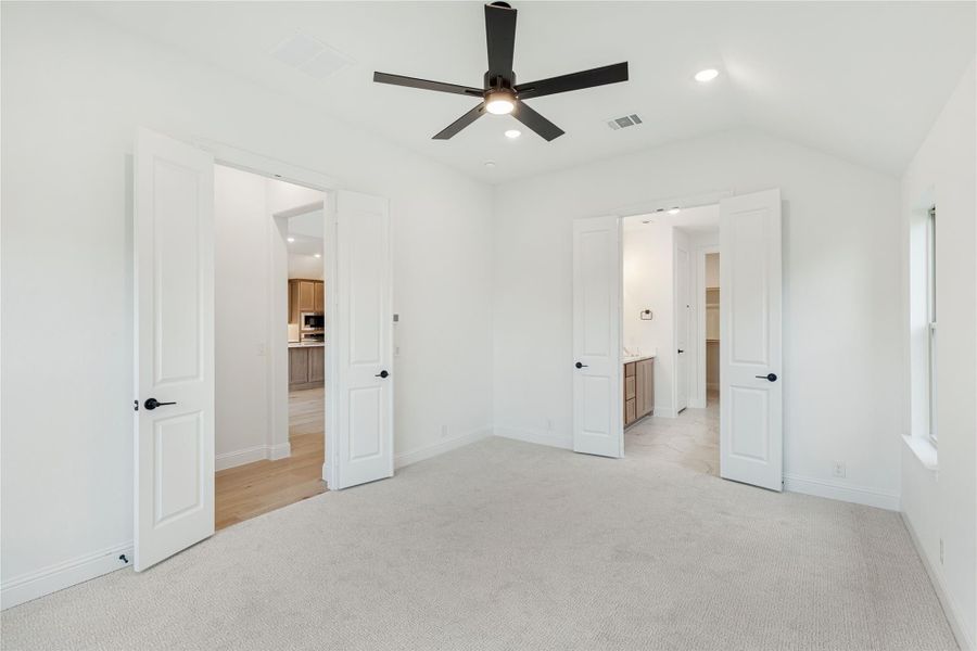 Empty bedroom with carpet, ceiling fan, and open doors leading to bathroom and hallway