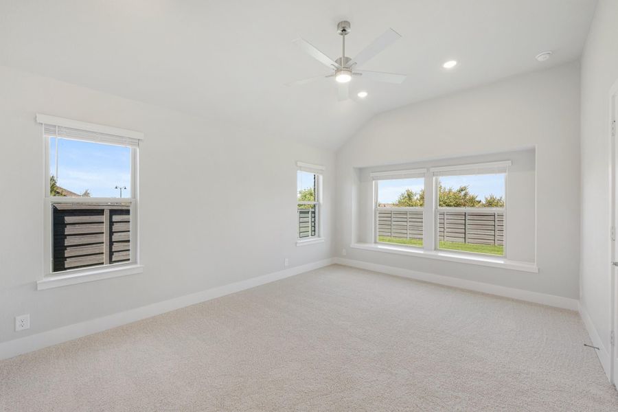 Empty bedroom with vaulted ceiling, ceiling fan, carpet flooring, and multiple windows with backyard views Empty bedroom with vaulted ceiling, ceiling fan, carpet flooring, and multiple windows with backyard views