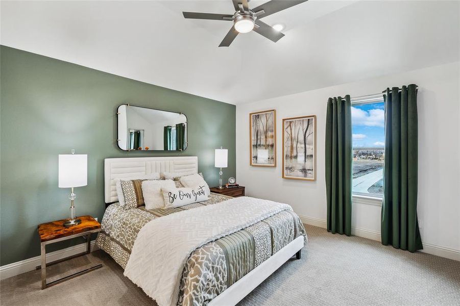 Vaulted ceiling bedroom featuring a contemporary ceiling fan with integrated lighting, soft grey carpeting, a prominent window with dark green drapes, and a striking accent wall