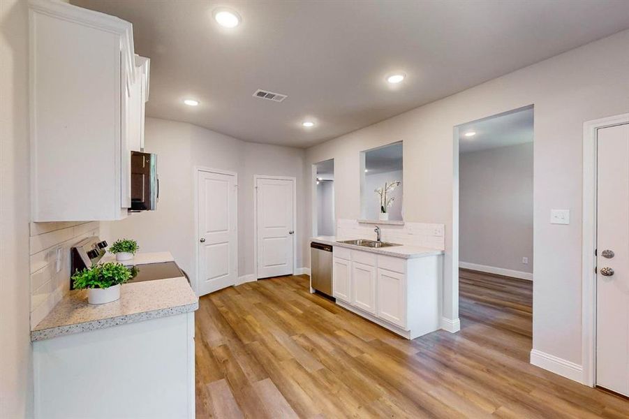 Kitchen featuring tasteful backsplash, appliances with stainless steel finishes, white cabinetry, light hardwood / wood-style floors, and sink