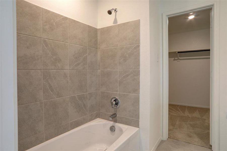 Full bathroom with washtub / shower combination, light colored carpet, light tile patterned floors, and a spacious closet