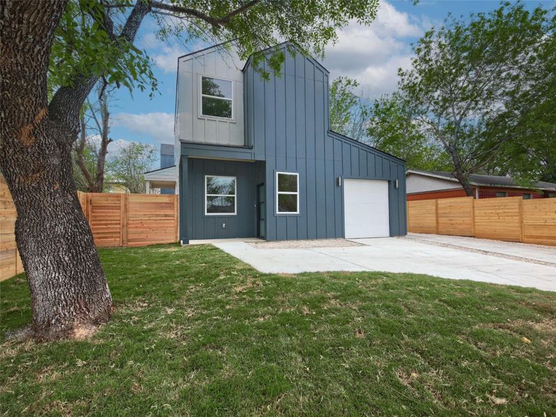 Back of property with board and batten siding, a fenced backyard, a garage, and concrete driveway