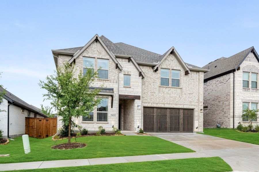 Two-story home with light stone exterior, two-car garage, and manicured front lawn with young tree Two-story home with light stone exterior, two-car garage, and manicured front lawn with young tree