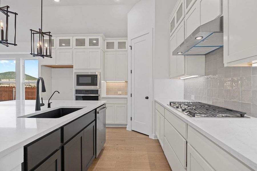Kitchen with ventilation hood, appliances with stainless steel finishes, white cabinets, light wood-style flooring, and decorative backsplash