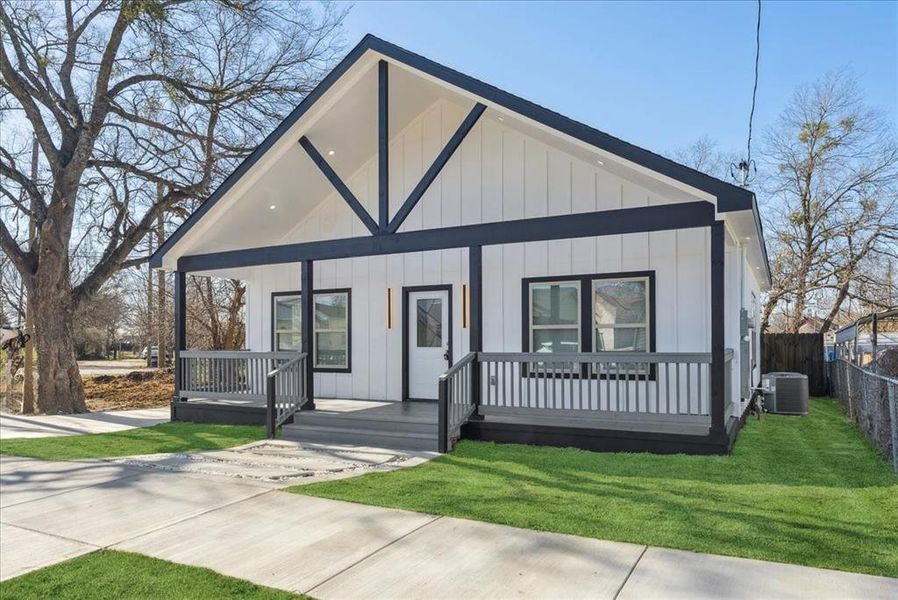 View of front facade with a porch, central AC unit, fence, board and batten siding, and a front yard