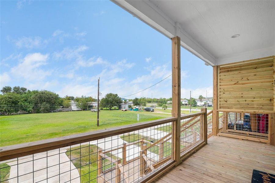 You're looking at a spacious covered deck with a wooden railing, offering a serene view.