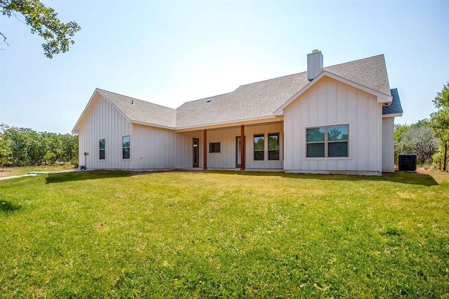 Back of house with a shingled roof, a patio, board and batten siding, a chimney, and a yard Back of house with a shingled roof, a patio, board and batten siding, a chimney, and a yard