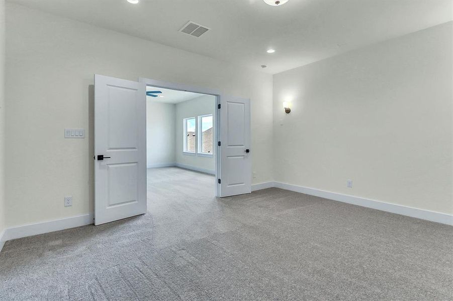 Carpeted interior room with white walls and baseboards, featuring recessed ceiling lighting, a wall sconce, and double panel doors with black hardware Carpeted interior room with white walls and baseboards, featuring recessed ceiling lighting, a wall sconce, and double panel doors with black hardware