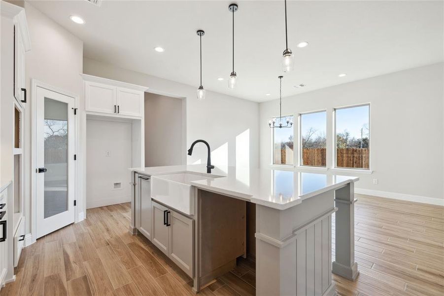 Kitchen with white cabinetry, sink, a notable chandelier, pendant lighting, and a kitchen island with sink