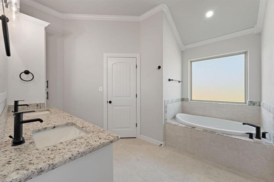 Bathroom featuring ornamental molding, double vanity, a garden tub, lofted ceiling, and recessed lighting