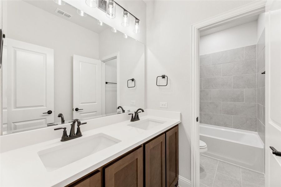 Bathroom with double sink vanity, dark wood cabinets, white countertop, and tiled tub-shower combo