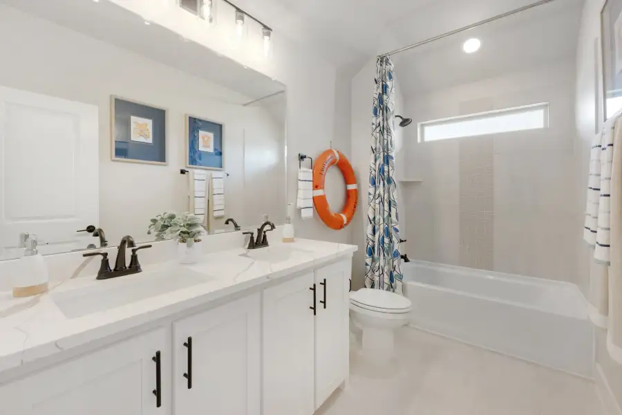 Bathroom with double white vanity, quartz countertop, and tub-shower combo with patterned curtain Bathroom with double white vanity, quartz countertop, and tub-shower combo with patterned curtain