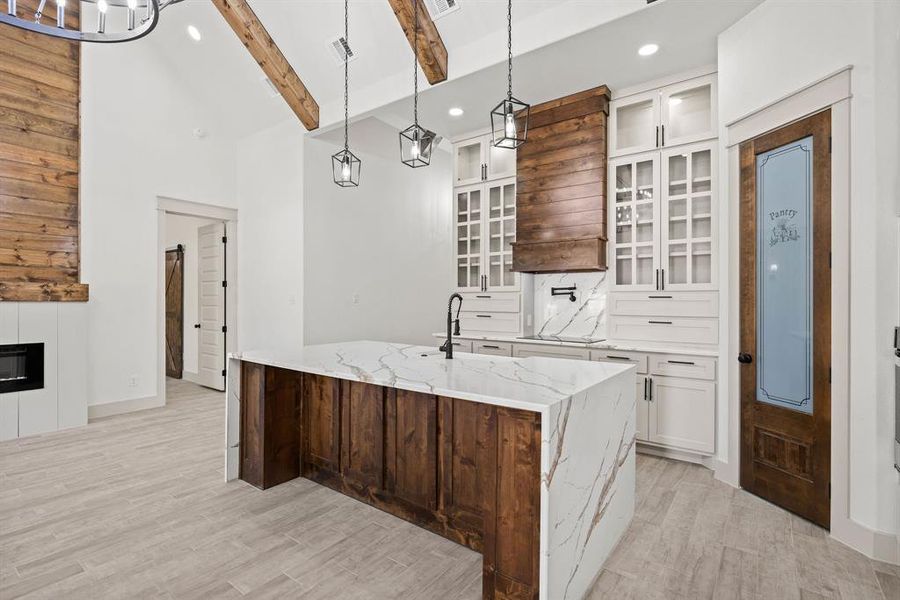 Kitchen with glass insert cabinets, white cabinets, light stone counters, recessed lighting, and light wood finished floors