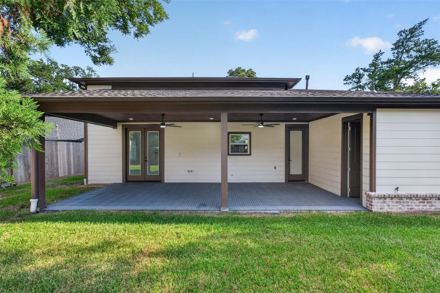 Spacious covered patio with ceiling fans and dual doors opens to a lush backyard, perfect for outdoor relaxation and entertaining.