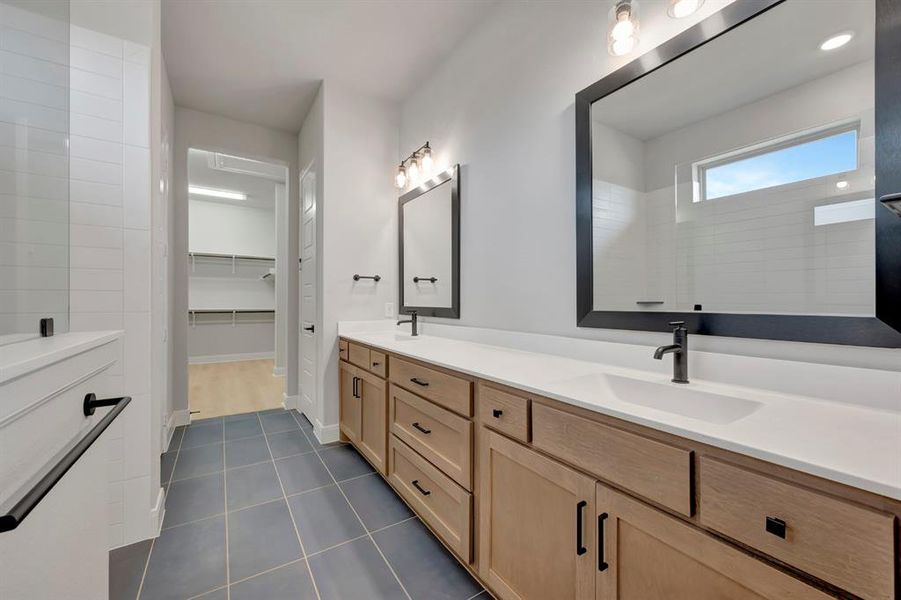 Full bathroom with double vanity, a spacious closet, and dark tile patterned flooring