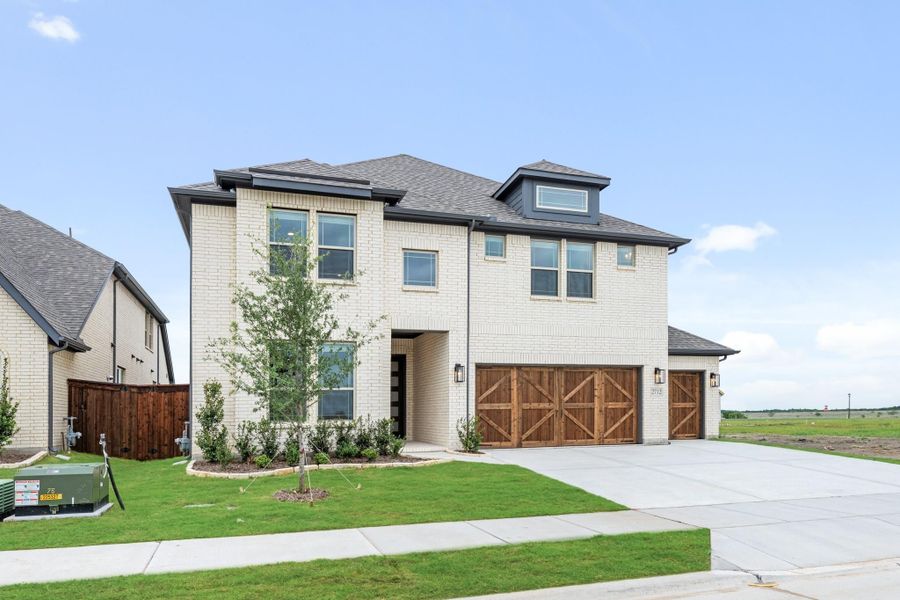 Two-story white brick home with wood garage doors, green lawn, and concrete driveway