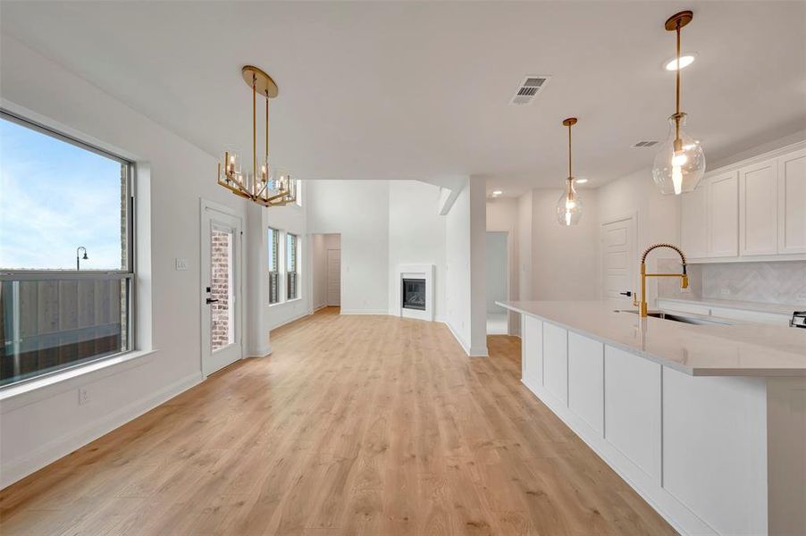 Kitchen with white cabinets, suspended lighting, light wood-type flooring, a fireplace, and a kitchen island with sink