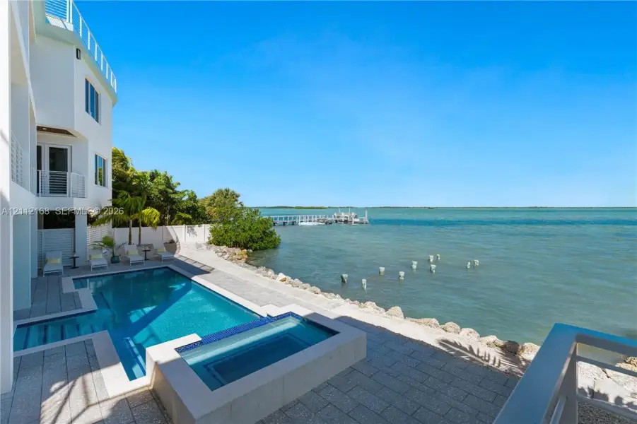 Waterfront property featuring an in-ground swimming pool, integrated spa, paved stone deck, and a private boat dock Waterfront property featuring an in-ground swimming pool, integrated spa, paved stone deck, and a private boat dock