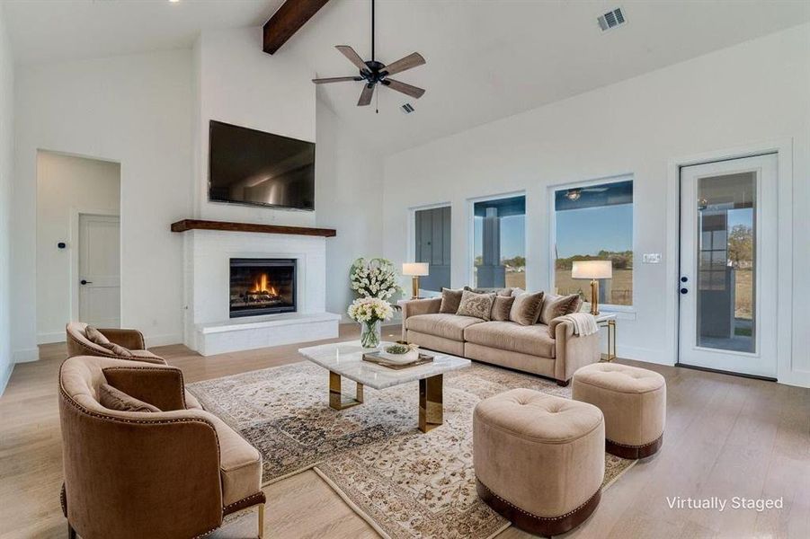 Living area featuring a warm lit fireplace, beamed ceiling, ceiling fan, high vaulted ceiling, and light wood-style floors