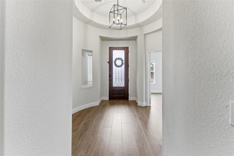 Entrance foyer featuring a tray ceiling, wood finished floors, a textured wall, and suspended lighting