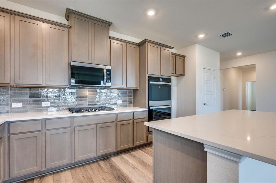 Kitchen with light wood finished floors, stainless steel appliances, decorative backsplash, recessed lighting, and light stone countertops Kitchen with light wood finished floors, stainless steel appliances, decorative backsplash, recessed lighting, and light stone countertops
