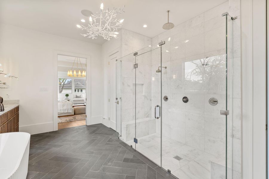 A large walk-in shower features floor-to-ceiling marble tile, dual shower heads, a built-in bench, and a glass enclosure that highlights the clean, luxurious design.