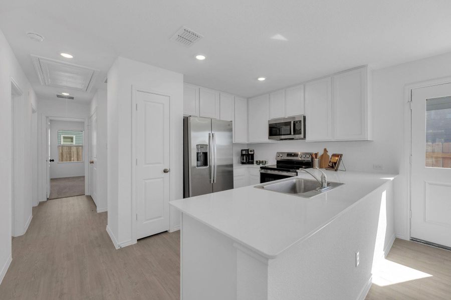 Kitchen featuring stainless steel appliances, white cabinetry, a peninsula, light vinyl floors, and recessed lighting.