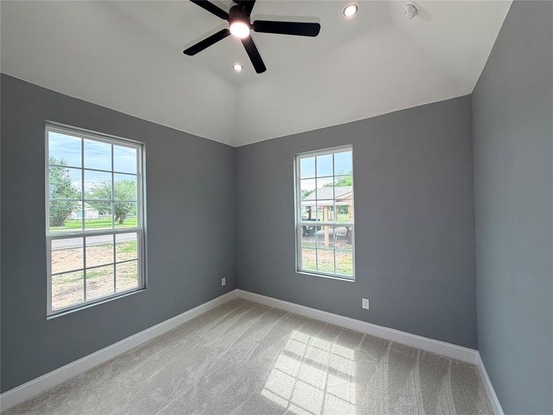 Vaulted ceiling bedroom featuring neutral carpeting, two large windows, a ceiling fan with integrated lighting, and recessed lighting Vaulted ceiling bedroom featuring neutral carpeting, two large windows, a ceiling fan with integrated lighting, and recessed lighting
