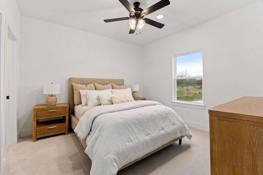 This cozy secondary bedroom features a dark stained ceiling fan, and a window with a pleasant outdoor view, creating a bright and inviting atmosphere.