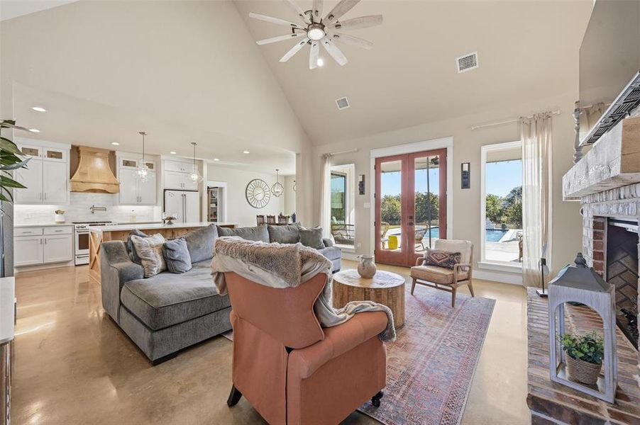 Living room with high vaulted ceiling, ceiling fan, french doors, finished concrete flooring, and a fireplace Living room with high vaulted ceiling, ceiling fan, french doors, finished concrete flooring, and a fireplace