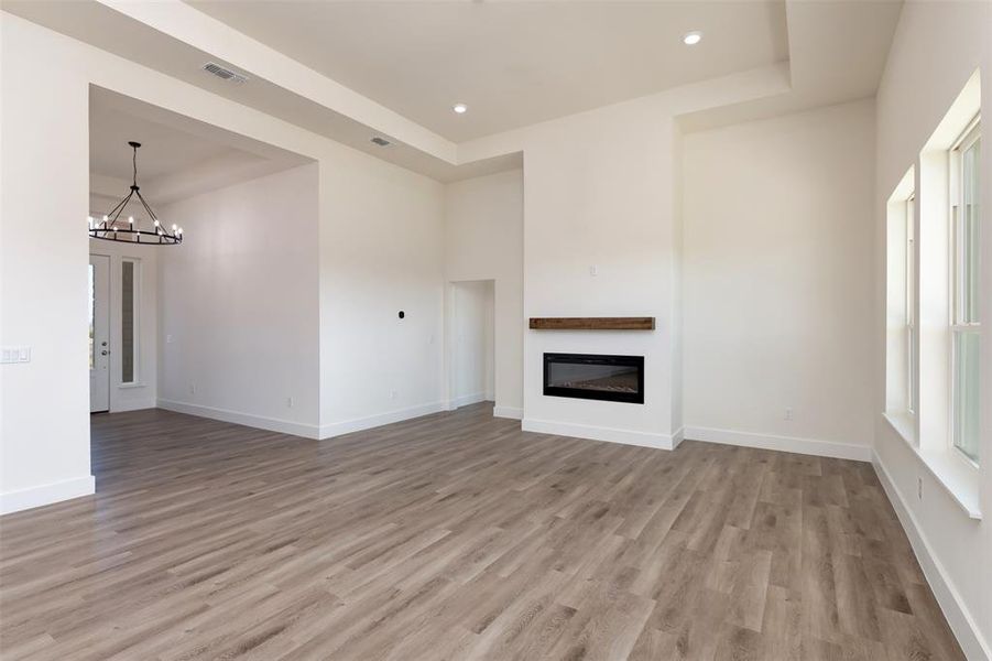 Unfurnished living room featuring baseboards, visible vents, a chandelier, and light wood finished floors