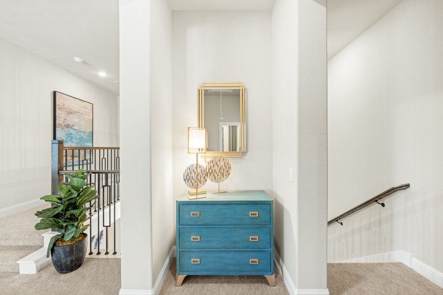Upstairs hallway landing with teal dresser, gold mirror, and staircase railing with potted plant nearby Upstairs hallway landing with teal dresser, gold mirror, and staircase railing with potted plant nearby