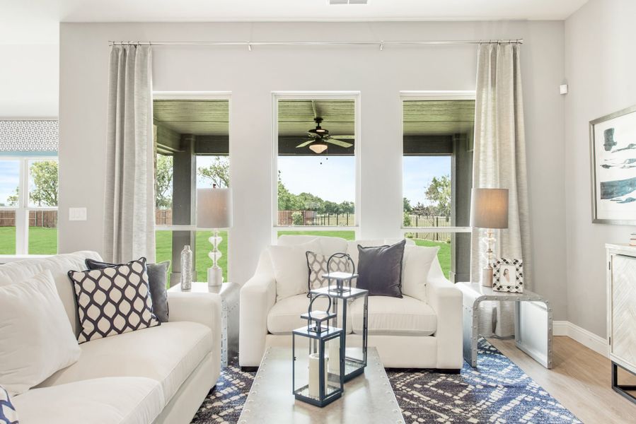 Living room with white sofas, blue patterned rug, and three large windows overlooking a covered patio and backyard.