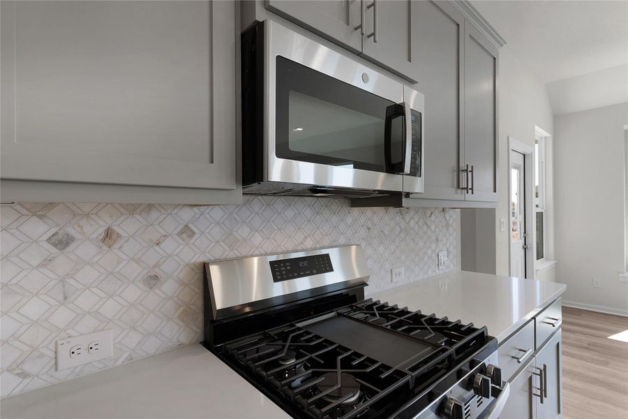 Kitchen featuring stainless steel appliances, gray cabinets, light stone counters, backsplash, and light wood-style floors