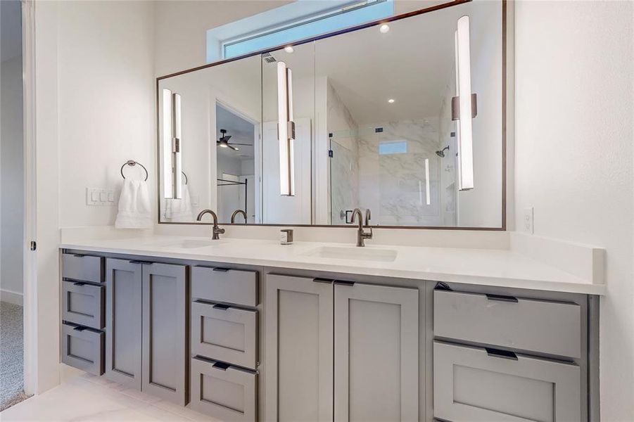 Bathroom with tiled shower, ceiling fan, and double sink vanity