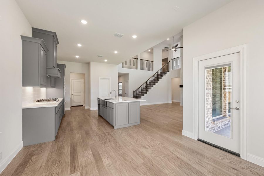 Open-concept kitchen with gray cabinets, center island, and hardwood floors leading to a staircase Open-concept kitchen with gray cabinets, center island, and hardwood floors leading to a staircase