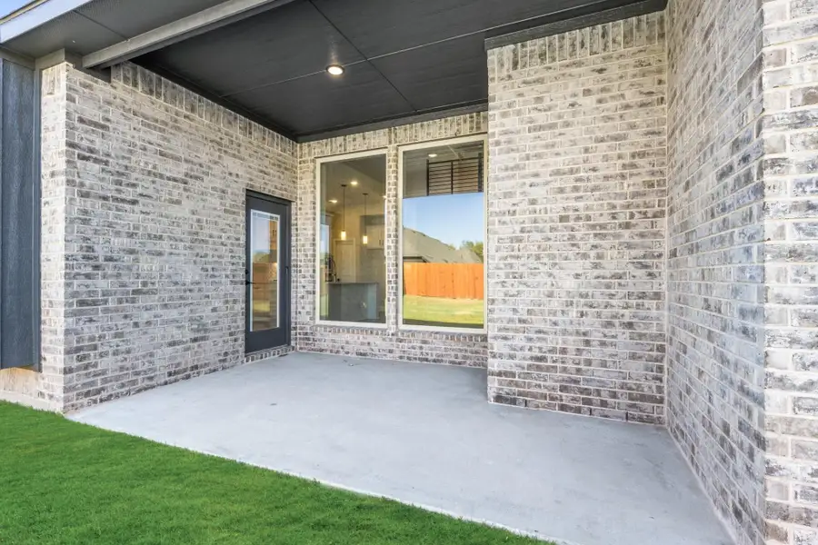 Covered back patio with concrete floor, light brick exterior, glass door, and large window overlooking green lawn. Covered back patio with concrete floor, light brick exterior, glass door, and large window overlooking green lawn.