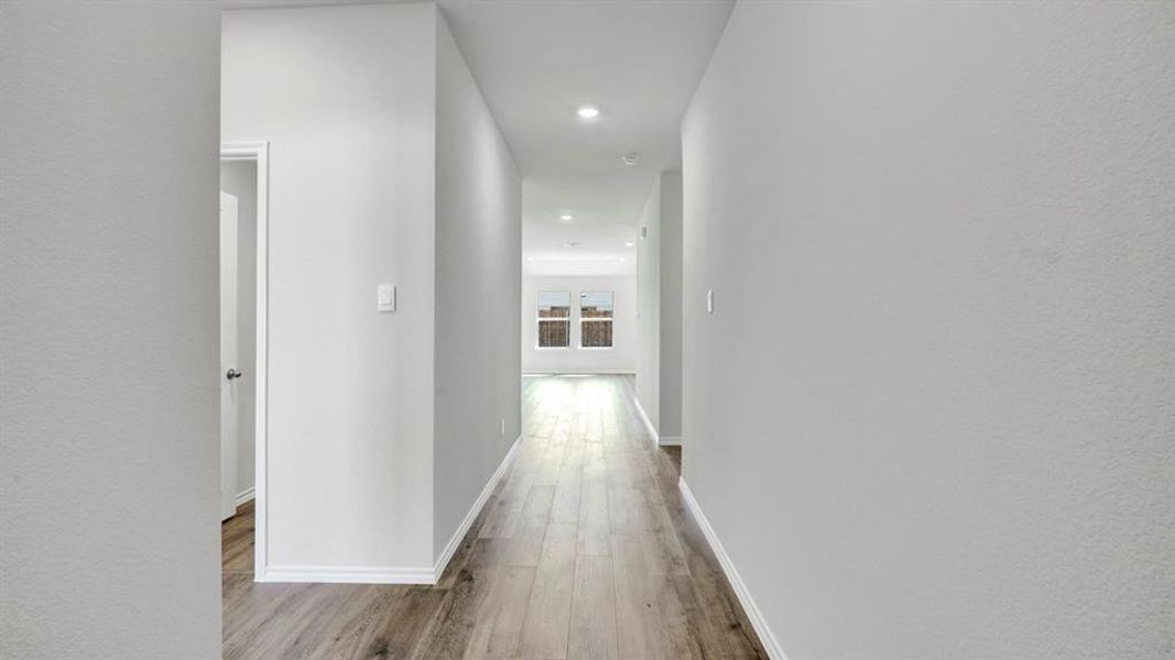 Hall with light wood finished floors, recessed lighting, and a textured wall