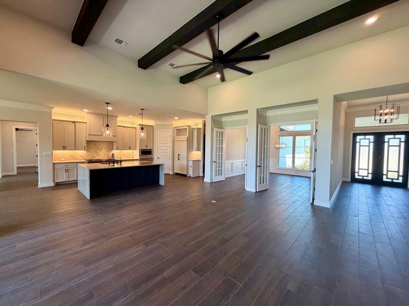 Rich wood-look flooring stretches beneath dramatic beamed ceilings in this open layout.