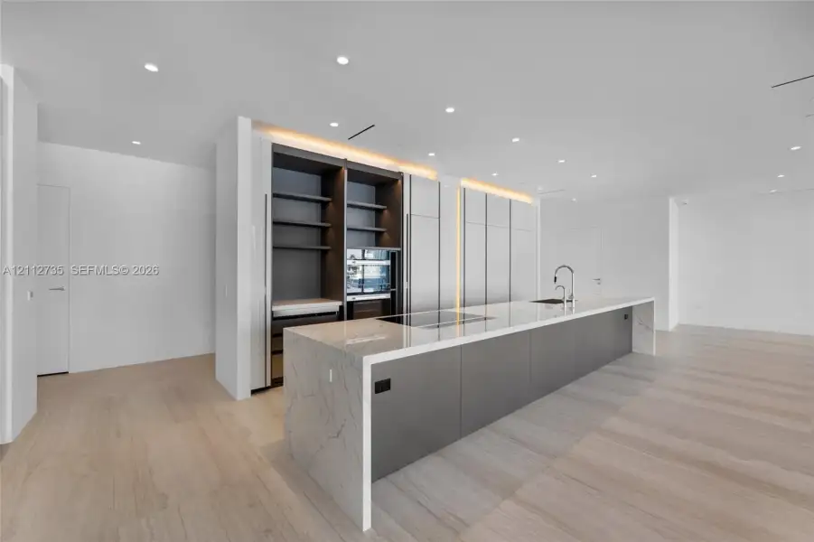 Modern kitchen featuring a waterfall-edge stone island, integrated cabinetry, wood-finish flooring, recessed lighting, and built-in appliances