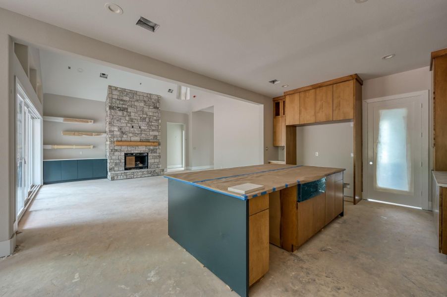 The open-concept kitchen and living area features a large kitchen island with wood cabinetry, a stone fireplace, and sliding glass doors leading outside. The room has high ceilings and built-in shelving.