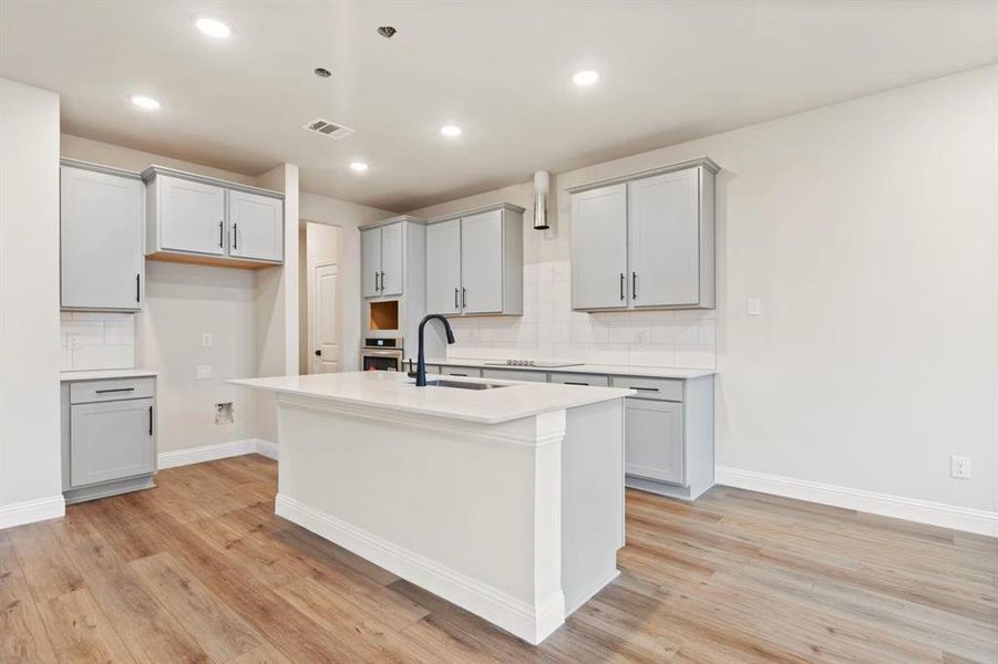 Kitchen featuring sink, gray cabinets, oven, and an island with sink