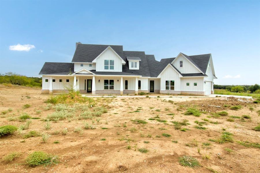 Modern inspired farmhouse with covered porch, board and batten siding, a shingled roof, and an attached garage Modern inspired farmhouse with covered porch, board and batten siding, a shingled roof, and an attached garage