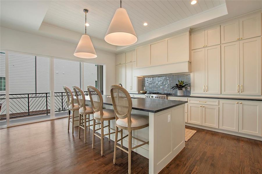 Kitchen featuring dark hardwood flooring, decorative light fixtures, a raised ceiling, and backsplash