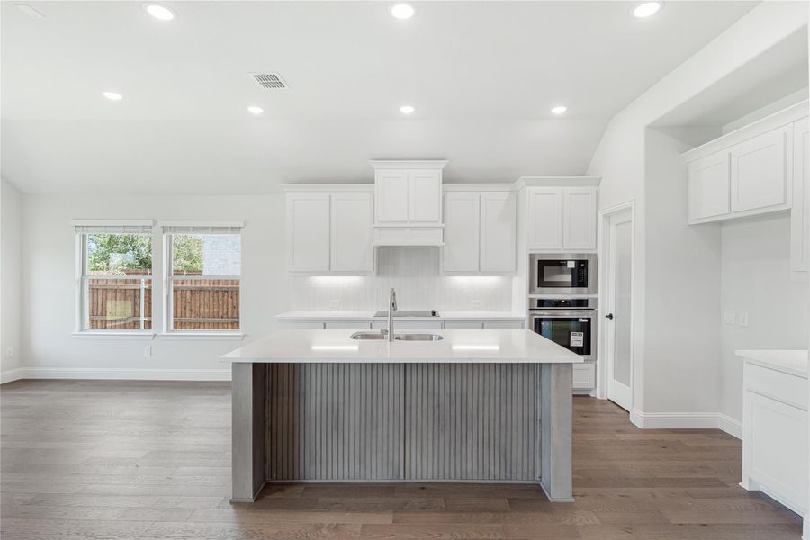 Kitchen with white cabinets, gray island with sink, stainless steel appliances, and hardwood floors