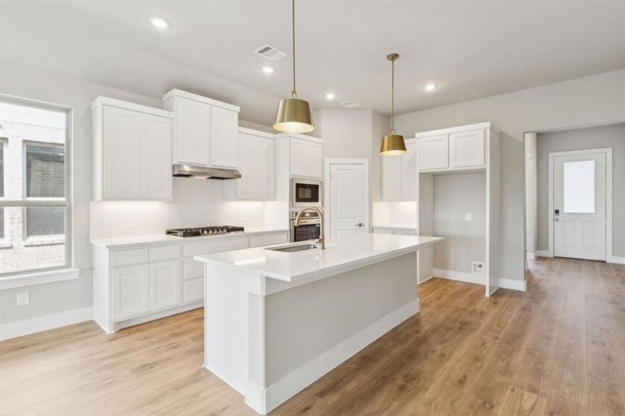 Kitchen featuring healthy amount of natural light, hanging light fixtures, tasteful backsplash, light wood-style floors, and recessed lighting