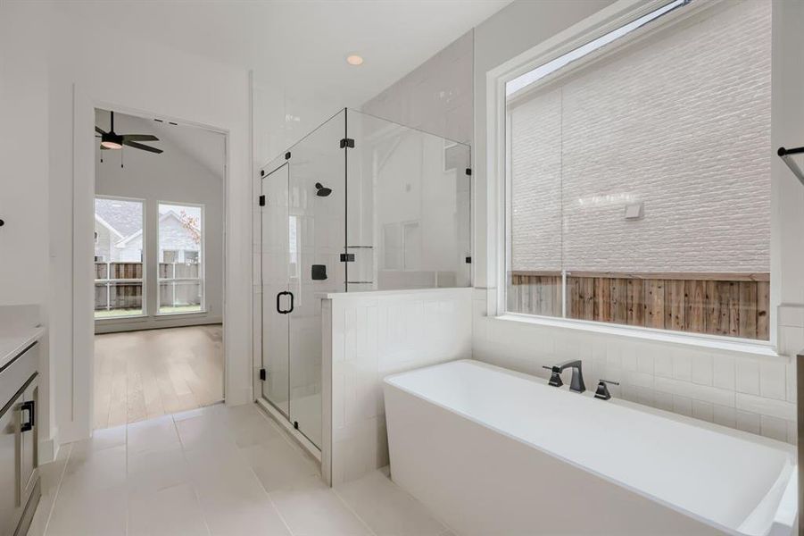 Modern bathroom featuring a freestanding tub with matte black fixtures, a glass-enclosed shower, white tile flooring, and a large window with privacy blinds Modern bathroom featuring a freestanding tub with matte black fixtures, a glass-enclosed shower, white tile flooring, and a large window with privacy blinds