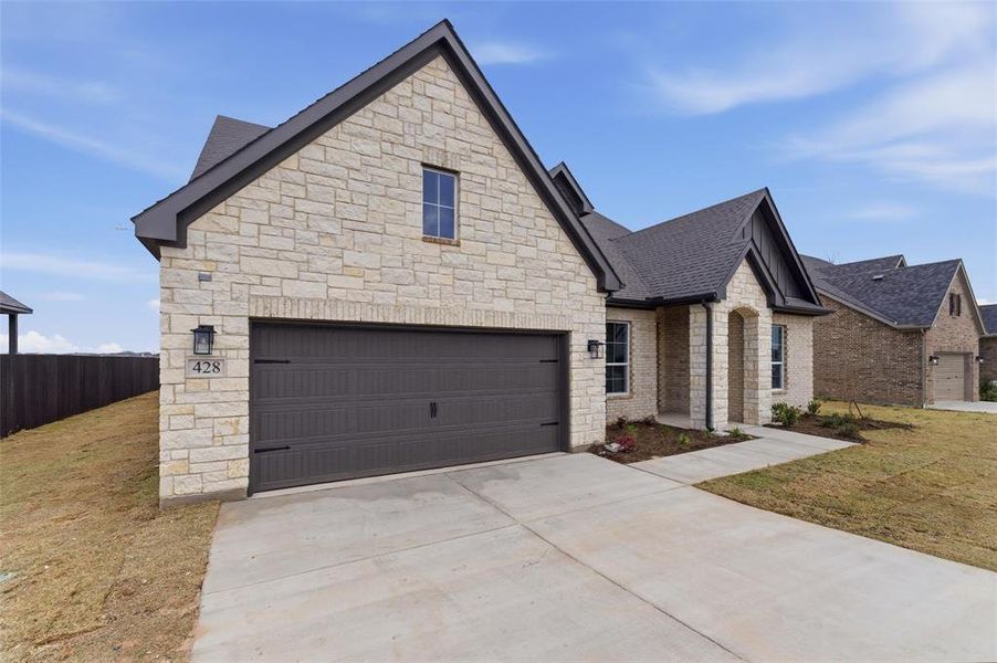 French country inspired facade featuring driveway, a garage, and stone siding