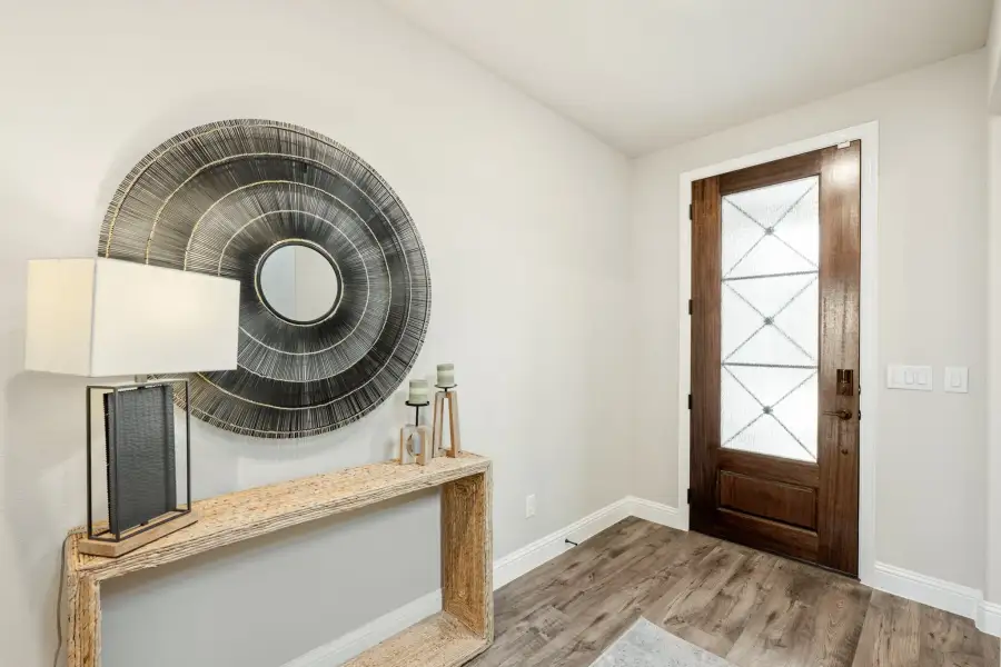 Home entryway with wood front door, glass panel, console table, and large round wall mirror on hardwood floors
